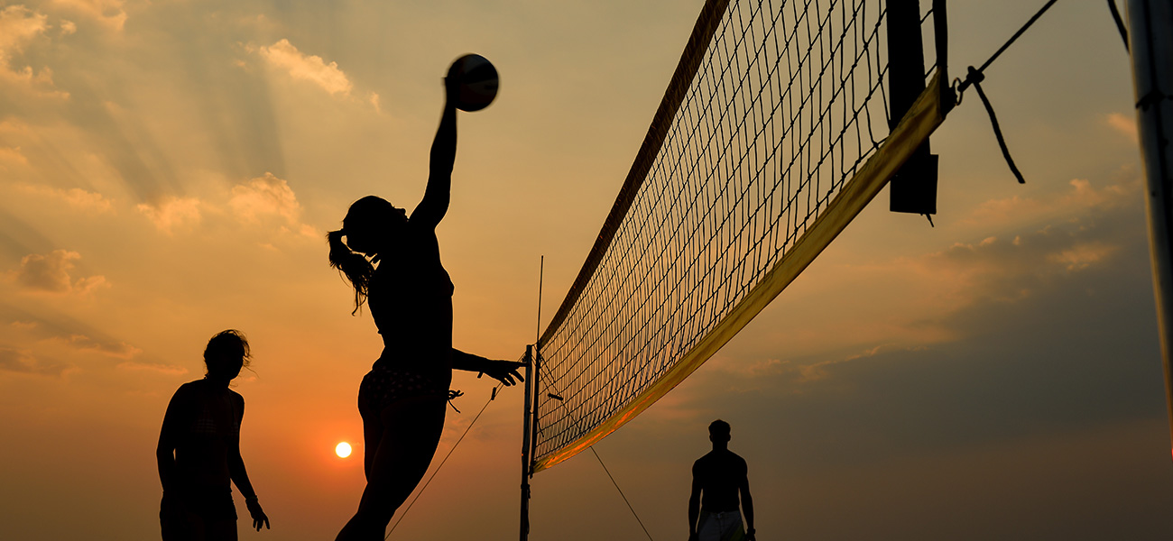 People playing beach volleyball at sunset.